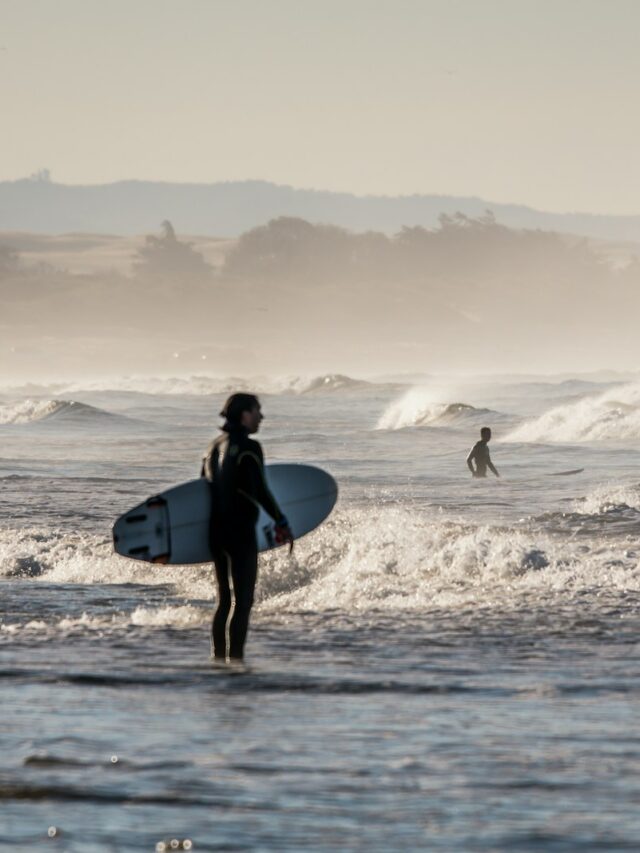 person holding white surfboard standing on body of water under gray sky during daytime